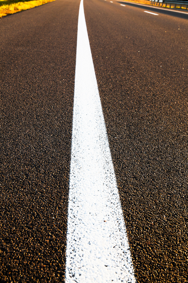 Close-up view of an empty asphalt road with a single straight white line running down the center, photographed at a low angle in daylight—quality found with top asphalt companies Cleveland Ohio trusts.