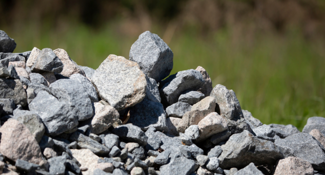 3 A pile of various-sized gray rocks and stones sits outdoors, hinting at materials ideal for ohio concrete recycling, with green grass and blurred vegetation in the background.